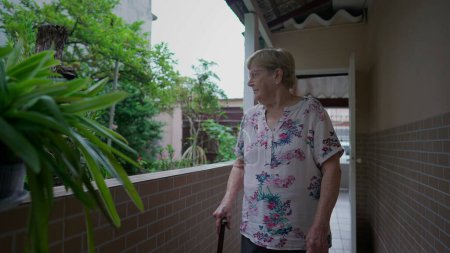 Téléchargez les photos : Femme âgée pensive Marcher à la maison en contemplant le jardin. Une personne âgée réfléchie dans les années 80 marche avec un bâton - en image libre de droit