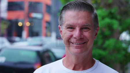 Foto de Retrato de un hombre alegre de mediana edad mirando a la cámara sonriendo mientras estaba de pie en la calle de la ciudad. Gris peludo amistoso mayor hombre persona - Imagen libre de derechos