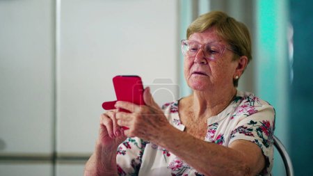 Foto de Señora mayor utiliza el dispositivo de teléfono inteligente en casa, la vejez estilo de vida doméstico celebración de la tecnología moderna mirando a la pantalla del teléfono - Imagen libre de derechos