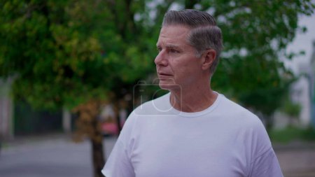 Photo for One contemplative senior man walking in city street observing urban surrounding. A caucasian middle-age male person strolling in sidewalk - Royalty Free Image