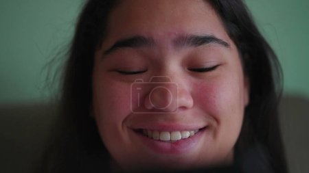Foto de Jovencita brasileña alegre reaccionar _ s positivamente al contenido en línea mientras sostiene el teléfono. Primer plano de una feliz diversa mujer asiática _ s cara sonriendo mensaje de lectura - Imagen libre de derechos