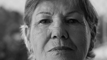 Foto de Resolute Senior Woman _ s Retrato en dramático blanco y negro. Cara de cerca mirando a la cámara. Mujer mayor con arrugas y expresión determinada en monocromático - Imagen libre de derechos