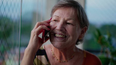 Téléchargez les photos : Heureuse femme âgée parlant au téléphone tenant smartphone dans l'oreille. Une personne âgée joyeuse en communication - en image libre de droit