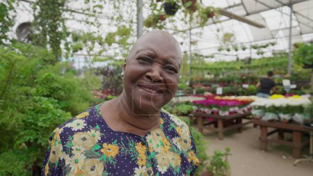 Téléchargez les photos : Femme âgée afro-américaine regardant la caméra debout à l'intérieur Flower Shop. Une femme noire femme plus âgée portrait visage proche - en image libre de droit