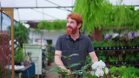 Téléchargez les photos : Jeune homme heureux avec panier explorant l'allée dans un magasin d'horticulture. Homme client achats pour les plantes à la boutique de jardin locale - en image libre de droit
