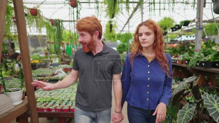 Photo for Exploring Flower Shop_ Redhead Couple Seeking Decorative Plants in Dynamic Tracking Shot. Young man and woman shopping for Flowers - Royalty Free Image