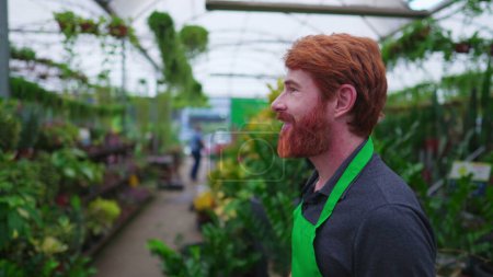 Photo for Happy redhead Young entrepreneur walking through Flower Shop. A male business Florist owner of Plant Store strolling through Horticulture environment - Royalty Free Image