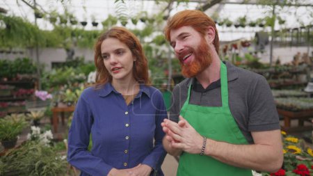 Téléchargez les photos : Un jeune homme fleuriste engagé à aider une cliente dans un magasin de fleurs local - en image libre de droit