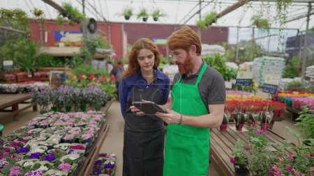 Photo for Male Staff Sharing Inventory Data on Tablet with Female Colleague in Flower Shop. Two Employees Engaging in Retail Tech Interaction. Local Business Concept - Royalty Free Image