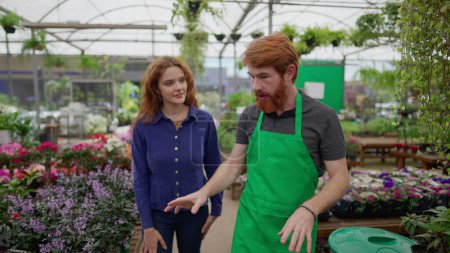 Photo for Redhead Man in Green Apron Assisting Female Customer in Local Flower Shop - Royalty Free Image