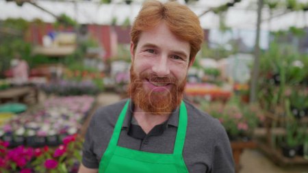 Photo for A male staff of Flower Shop holding tablet device while standing inside local business smiling at camera. Young redhair man employee wearing apron and using modern technology - Royalty Free Image