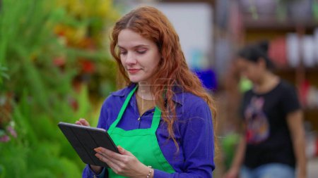 Foto de Evaluación de Inventario por Gerente Femenina en Tienda de Plantas Vibrantes. Tech-Savvy Mujer joven Optimización de las operaciones de la tienda de negocios - Imagen libre de derechos