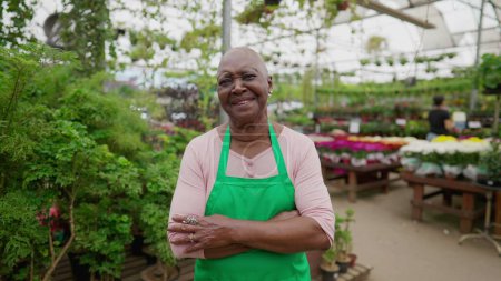 Photo for A happy black older woman employee standing inside Flower Shop wearing Green Apron. Portrait face close-up of a senior worker - Royalty Free Image