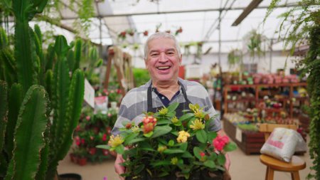 Foto de Propietario de negocio masculino mayor alegre amistoso de la tienda de la planta que lleva las flores Trabajando mayor en la tienda de jardinería local - Imagen libre de derechos