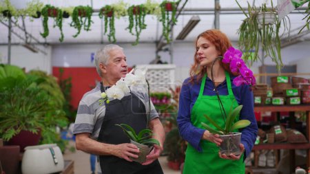 Foto de Personal de Horticultura caminando con flores en el pasillo de la tienda. Mujer joven y hombre mayor en delantales Plantas de transporte en pequeñas empresas Floristería - Imagen libre de derechos