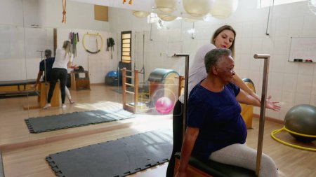 Téléchargez les photos : Une femme âgée noire reçoit un entraînement en santé de la colonne vertébrale de la part d'un instructeur de Pilates en studio - en image libre de droit