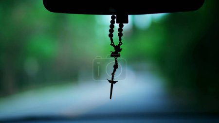 Photo for Christian Cross hanging by car_s rear view mirror while driving on road in motion - Royalty Free Image