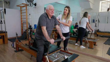 Téléchargez les photos : Homme âgé dans la routine d'entraînement de colonne vertébrale, session de studio Pilates Entraîné par une instructrice - en image libre de droit