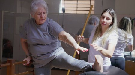 Téléchargez les photos : Entraîneuse Pilates guidant une femme âgée à étirer sa jambe en classe de physiothérapie - en image libre de droit