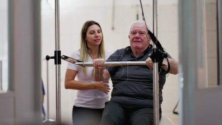 Téléchargez les photos : Physiothérapeute féminine aidant l'homme âgé sur Pilates Machine - en image libre de droit