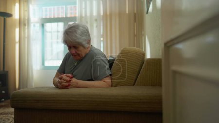 Téléchargez les photos : Femme âgée pleine d'espoir PRIER à la maison dans la solitude. Fidèle vieille femme caucasienne avec les mains serrées ayant la foi - en image libre de droit