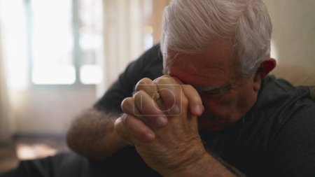 Foto de Esperanzado anciano rezando en casa en soledad. Fiel mayor hombre caucásico persona con las manos apretadas teniendo FE - Imagen libre de derechos