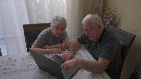 Photo for Elderly couple using laptop at home, old age and modern technology. Seniors looking at computer screen pointing at online content - Royalty Free Image