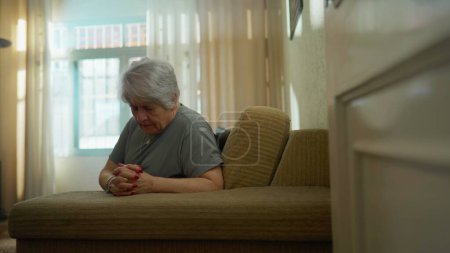 Téléchargez les photos : Femme âgée pleine d'espoir PRIER à la maison dans la solitude. Fidèle vieille femme caucasienne avec les mains serrées ayant la foi - en image libre de droit