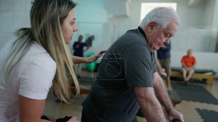 Foto de Instructor de Pilates femenino que entrena al anciano para hacer ejercicio con la máquina dentro del estudio de fisioterapia - Imagen libre de derechos