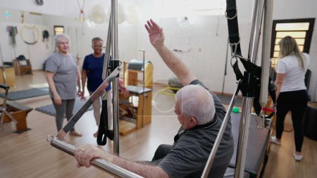 Téléchargez les photos : Pilates Coach aider l'homme âgé à exercer dans Pilates Studio, séance de physiothérapie de groupe avec les personnes âgées, entraînement de santé de la colonne vertébrale-SD - en image libre de droit
