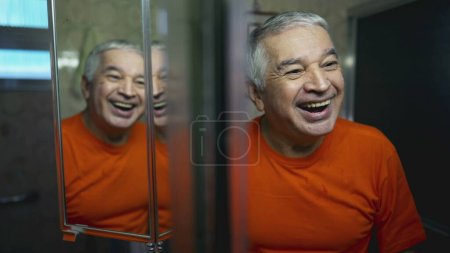 Téléchargez les photos : Heureux homme âgé se regardant dans le reflet miroir. Émotion joyeuse de la personne âgée riant et souriant dans le rituel du matin - en image libre de droit