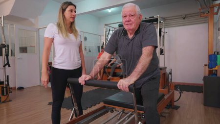 Photo for Older man exercising in Pilates studio being oriented by female coach. Senior person taking care of spine health - Royalty Free Image