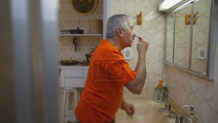 Téléchargez les photos : Candid senior homme rasage barbe en face du miroir dans la salle de bain. Authentique vie réelle vieillesse style de vie domestique de la personne âgée rituel du matin - en image libre de droit