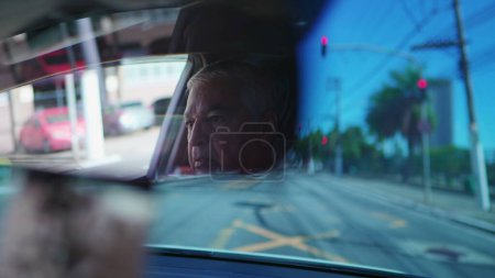 Téléchargez les photos : Conducteur principal vu à travers le rétroviseur d'une voiture qui attend dans la lumière rouge. Un homme plus âgé attend le feu vert - en image libre de droit