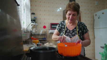Téléchargez les photos : Grand-mère traditionnelle préparant le repas, femme âgée engagée dans la cuisine à la maison - en image libre de droit