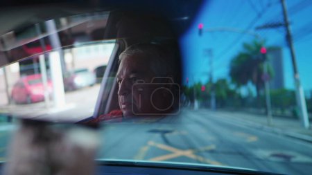 Foto de Conductor senior visto a través del espejo retrovisor de un coche esperando en la luz roja. Hombre mayor espera luz verde - Imagen libre de derechos