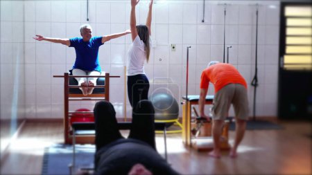Photo for Guided Fitness Scene of Pilates Instructor Assisting Seniors in a Group Class for Better health. Candid woman raising arms stretching and guiding students to exercise - Royalty Free Image