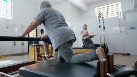 Téléchargez les photos : Dos de la femme âgée utilisant Pilates Machine pour étirer le corps. Séance d'entraînement pour personnes âgées - en image libre de droit