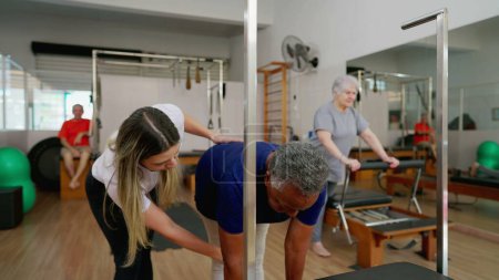 Foto de Instructora entrenando a una anciana para estirar el cuerpo en la sesión de Pilates. Persona que cuida la salud de la columna vertebral - Imagen libre de derechos
