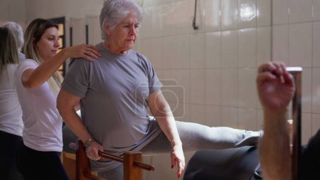 Photo for Female Pilates Coach guiding a senior woman to stretch body in physiotherapy class. Old age workout routine health and wellbeing lifestyle - Royalty Free Image