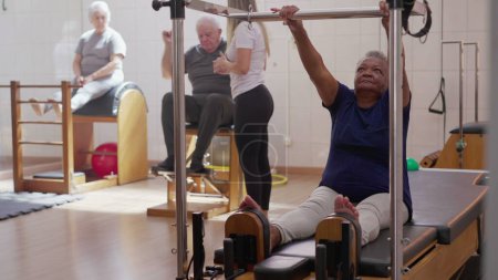 Téléchargez les photos : Exercice senior en Pilates Group Class, une femme noire qui utilise une machine pour renforcer son corps. Vieillesse entraînement mode de vie - en image libre de droit