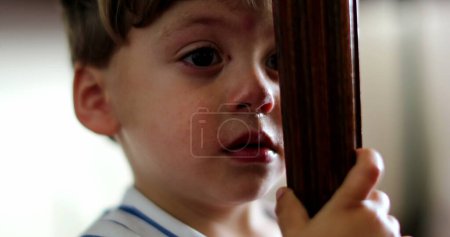 Foto de Niño temeroso escondido detrás de muebles sintiendo miedo niño tener miedo - Imagen libre de derechos