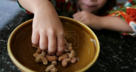 Photo for Little girl grabbing cashew nuts from bowl kid eating healthy snack - Royalty Free Image