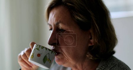 Téléchargez les photos : Candid senior femme sirotant du café le matin - en image libre de droit