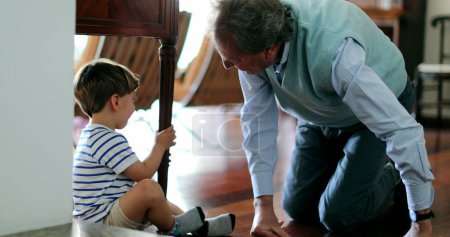 Téléchargez les photos : Grand-père empathique tendre la main pour blesser émotionnellement enfant caché sous la table - en image libre de droit