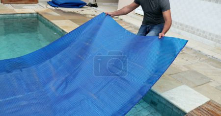 Téléchargez les photos : Homme enlevant la couverture de piscine et protecteur pliant - en image libre de droit