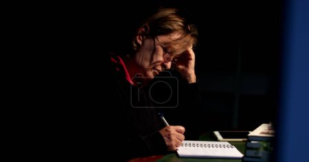 Foto de Pensativa persona mayor escribiendo en papel por la noche mujer mayor tomando notas - Imagen libre de derechos