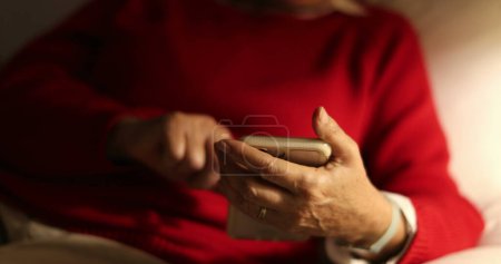 Téléchargez les photos : Senior femme lecture message tenant smartphone appareil la nuit assis sur le canapé - en image libre de droit