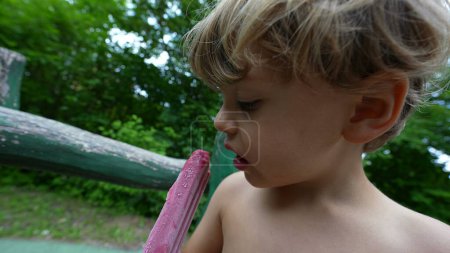 Téléchargez les photos : Enfant manger de la crème glacée dehors pendant la journée d'été - en image libre de droit