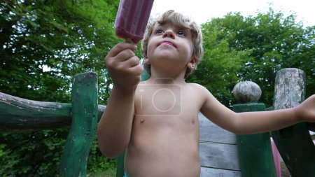Téléchargez les photos : Petit enfant manger de la crème glacée pendant la chaude journée d'été - en image libre de droit